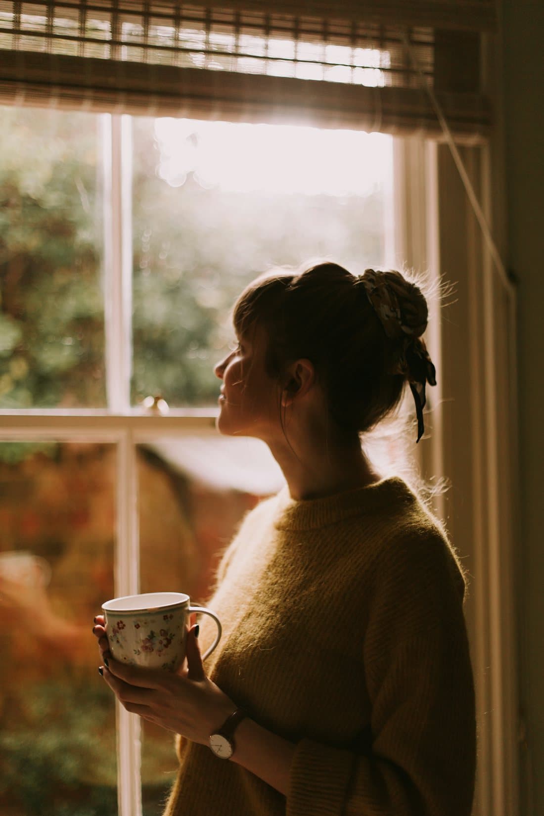 Woman holding a cup of tea by a sunlit window in a calm morning moment