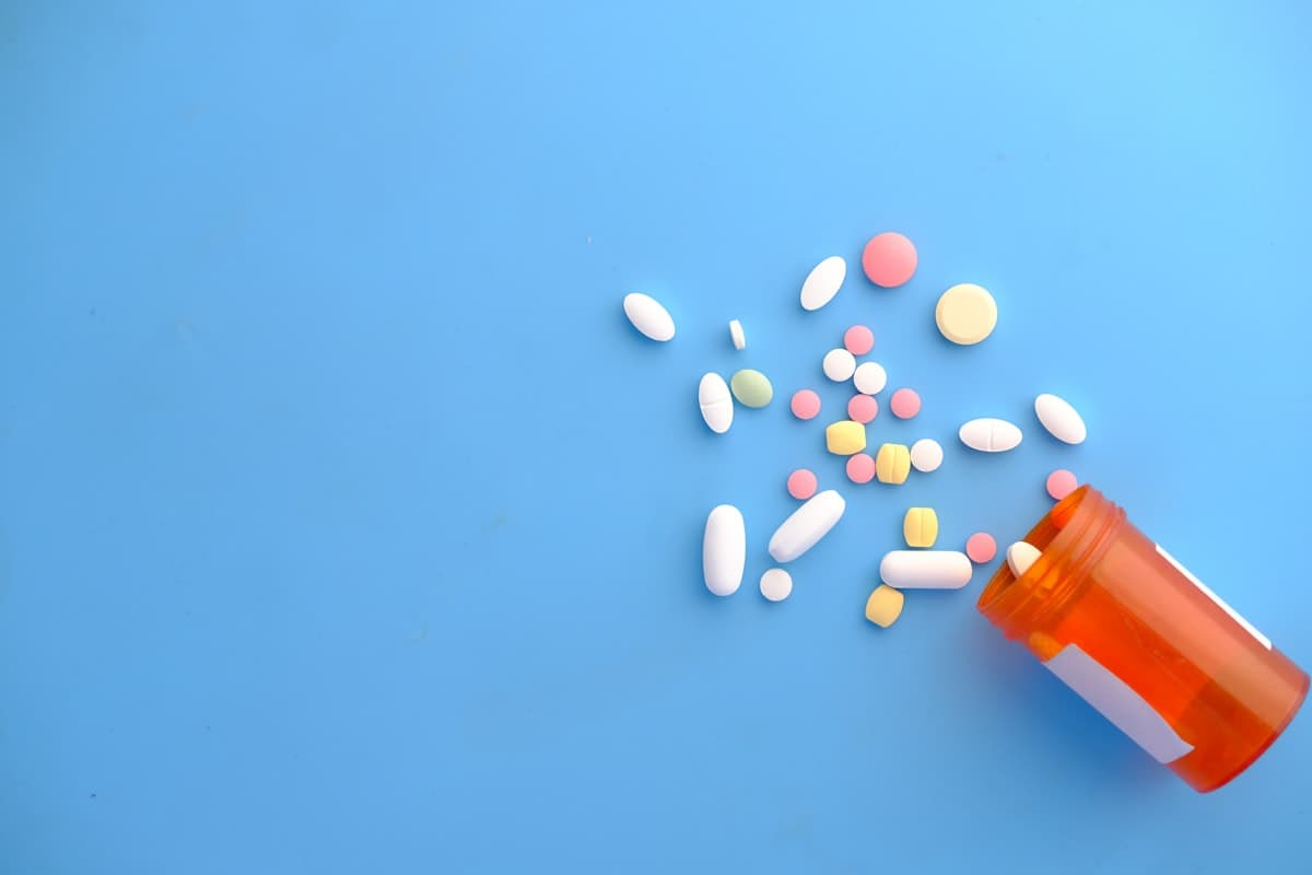 A small handful of pastel tablets beside an open bottle on a soft blue background